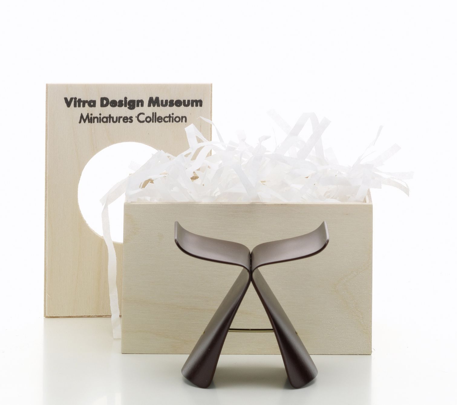 Vitra Butterfly Stool Miniatur Hocker (1954) vor Holzkiste mit Füllmaterial. Designklassiker für Sammler.