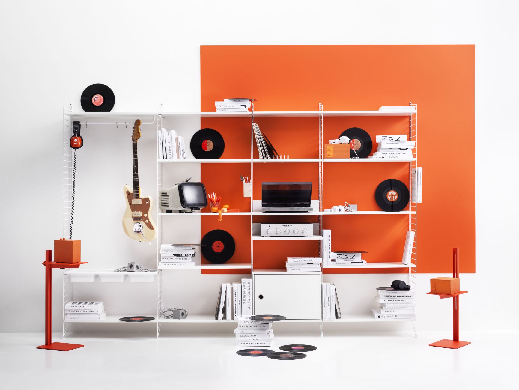 Weißes String Regalsystem mit Schallplatten, Büchern und Gitarre vor orangefarbenem Hintergrund. Wohnzimmer Wandregal für Musikliebhaber.