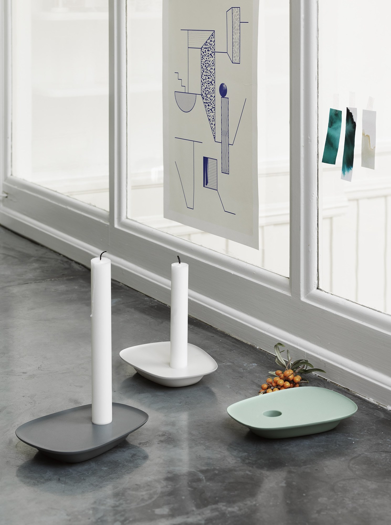 Drei Muuto Float Kerzenhalter in Grau, Weiß und Mintgrün mit weißen Kerzen.