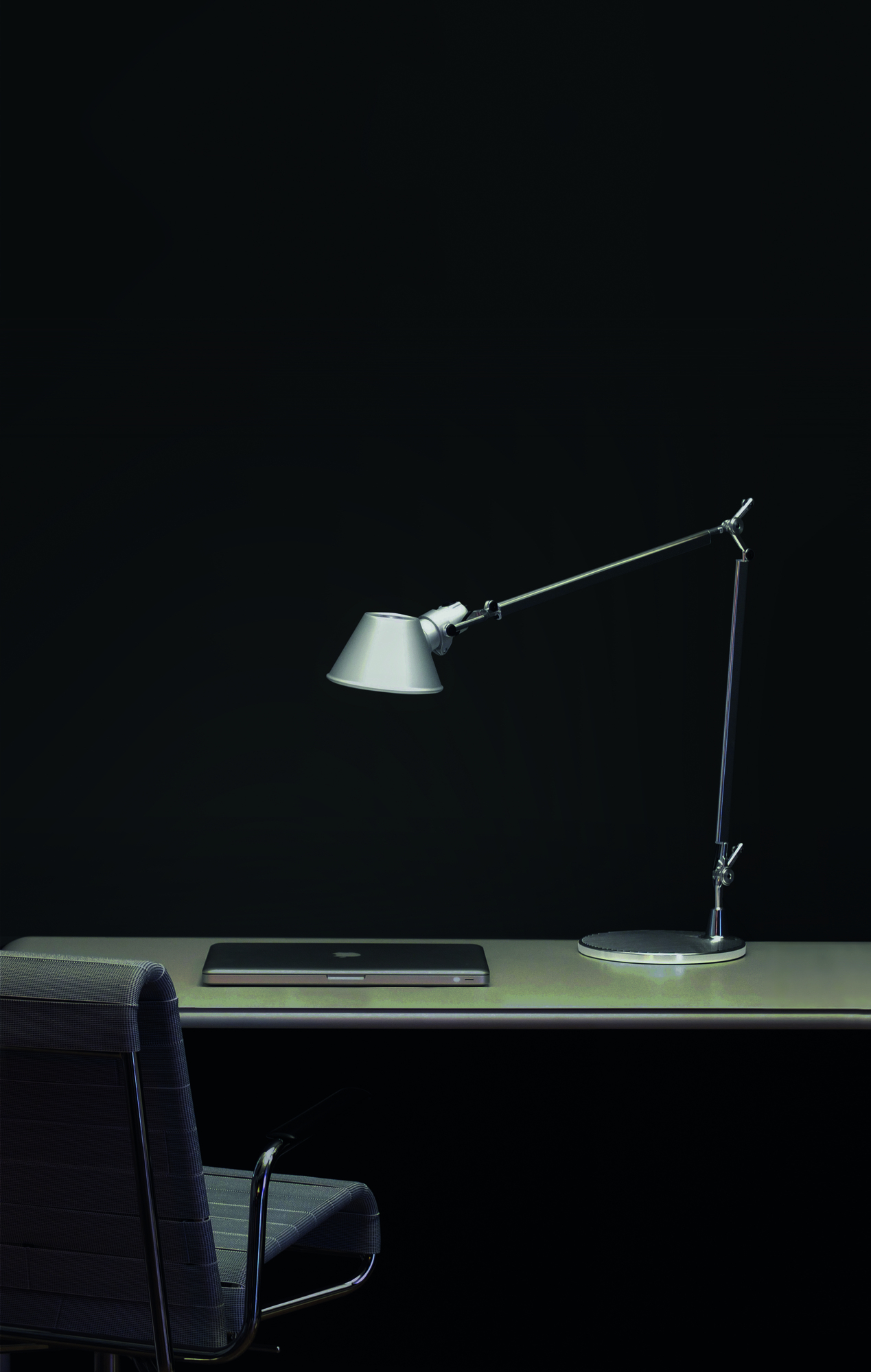 Silberne Tolomeo LED Tischleuchte von Artemide auf Schreibtisch mit Laptop und Bürostuhl vor schwarzem Hintergrund.