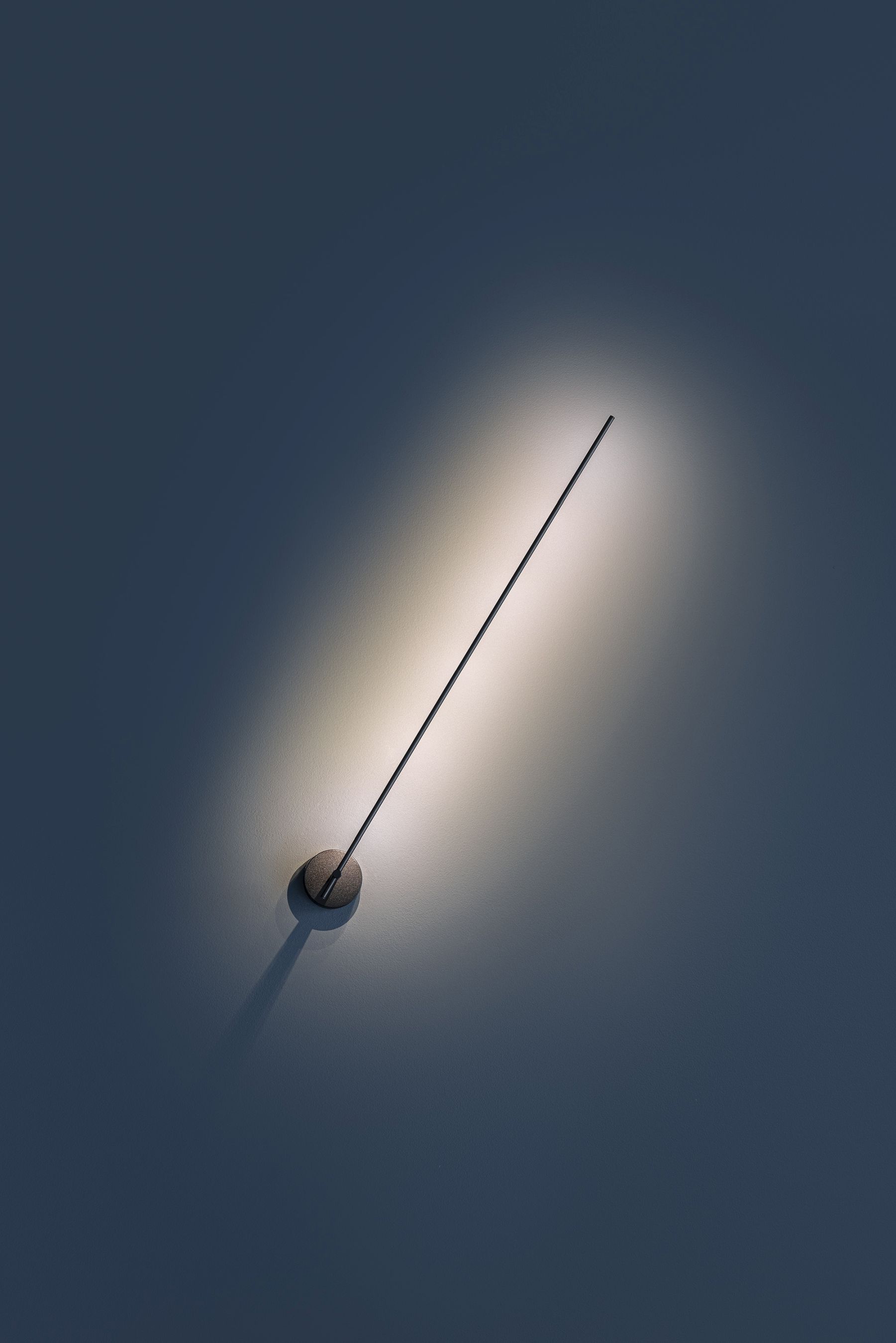 Light Stick Wandleuchte von Catellani & Smith, modernes Design mit warmem Lichtkegel an dunkler Wand.