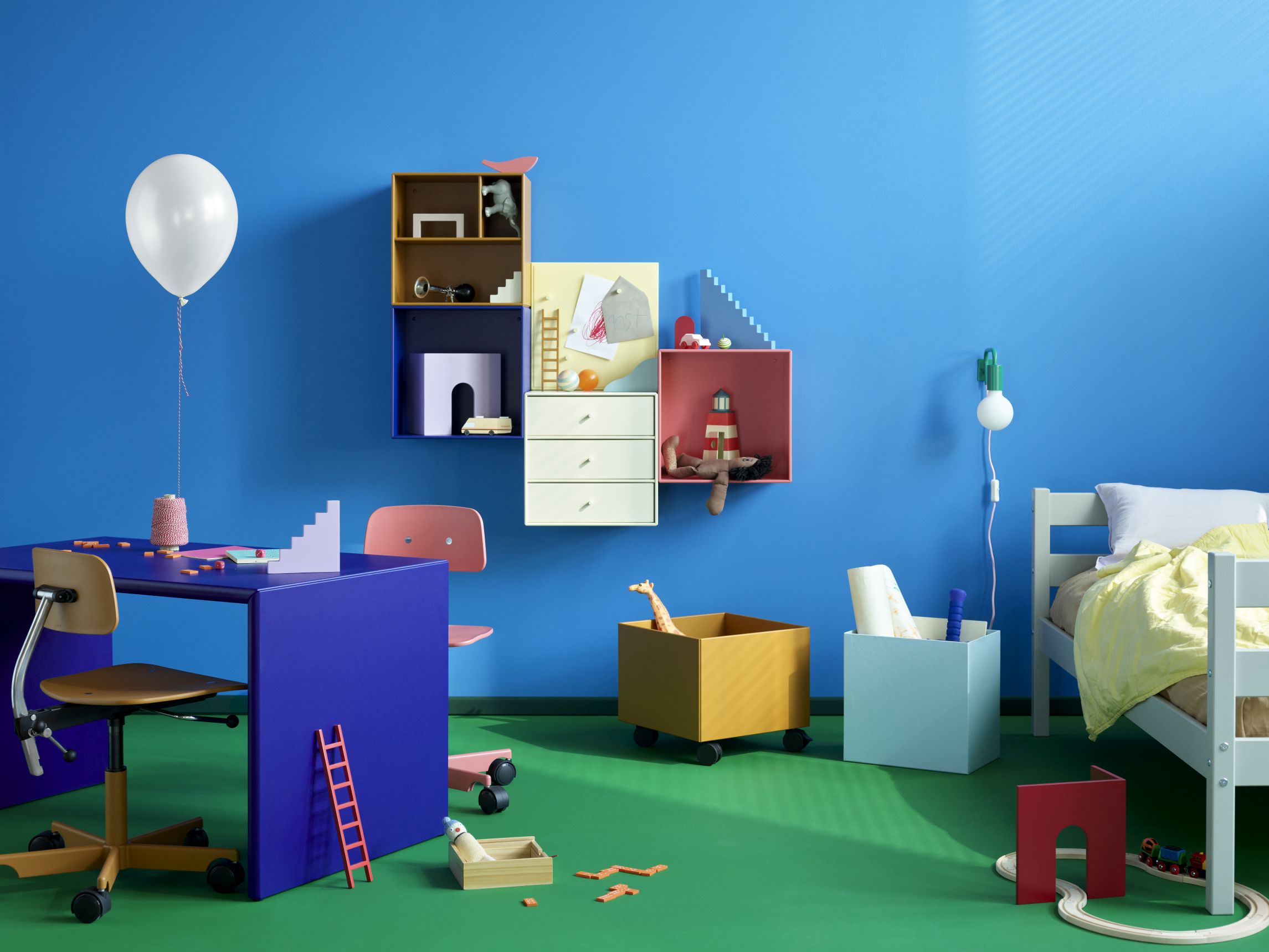 Kinderzimmer mit Kevi Kids Drehstuhl, Schreibtisch, Bett und bunten Spielsachen vor blauem Hintergrund.