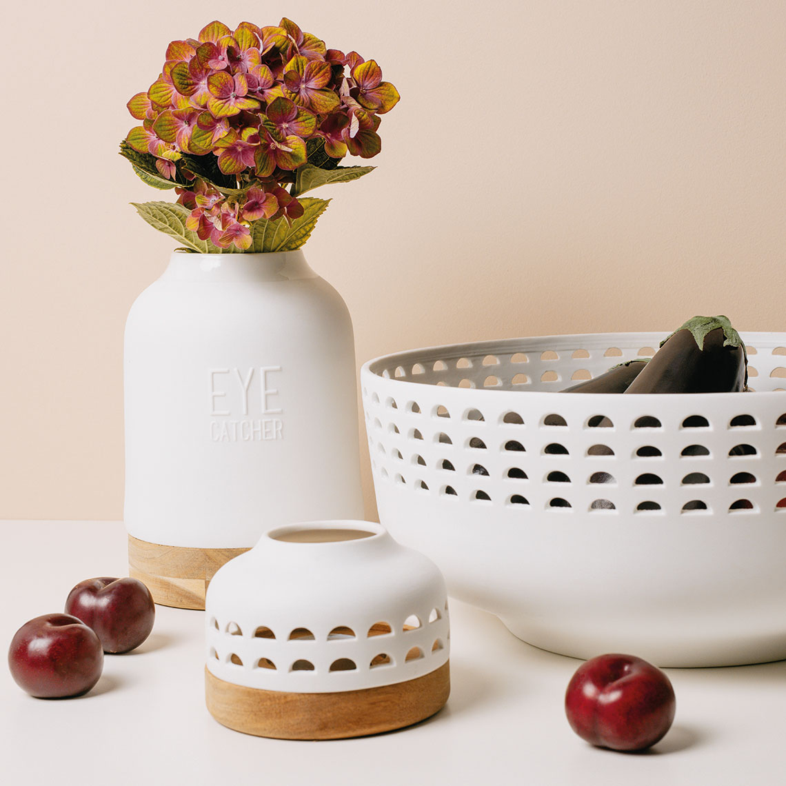 Weiße Eyecatcher Vase von Räder mit Blumen, dekorative Schale und Pflaumen auf hellem Untergrund.