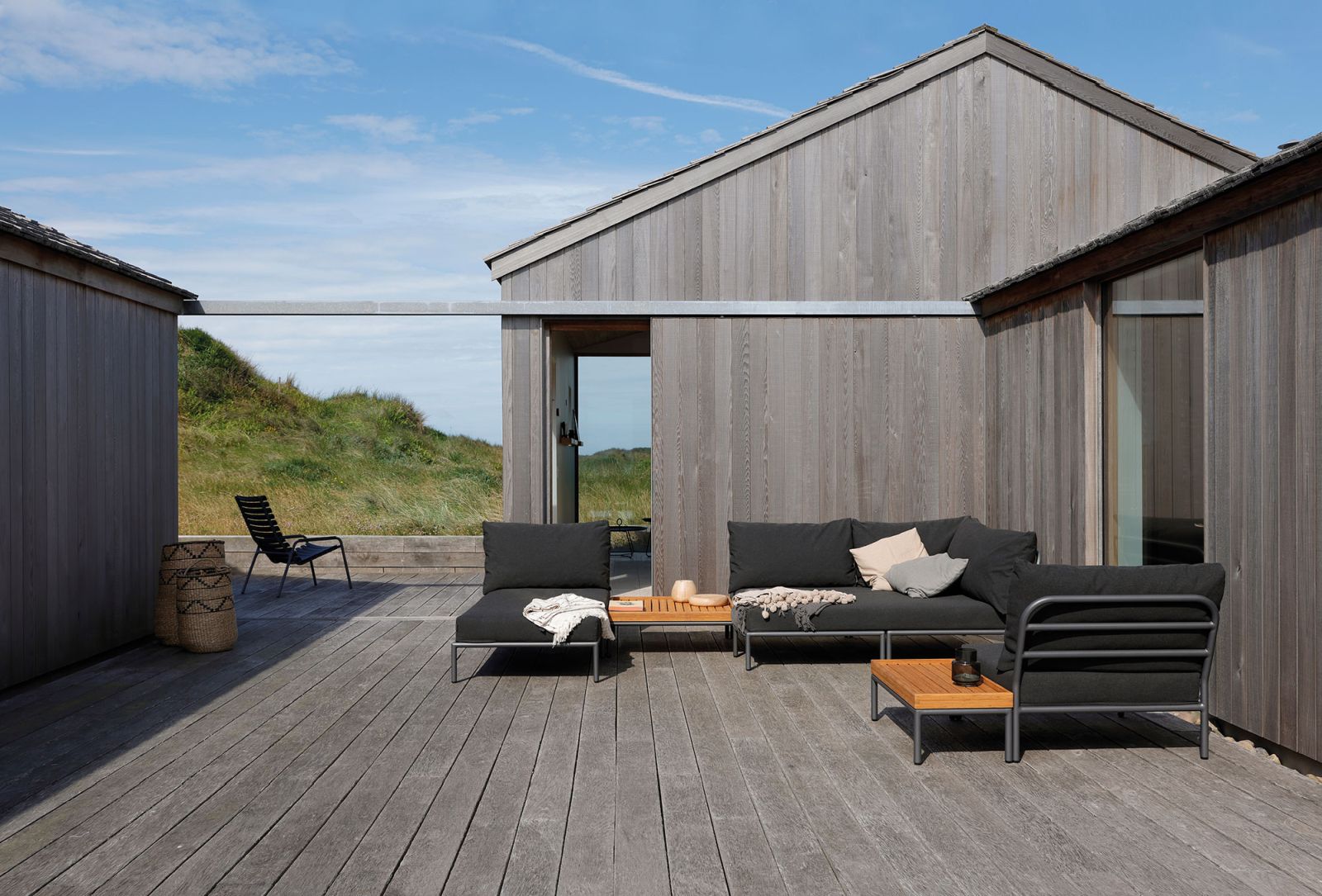 Houe Level Cozy Corner Outdoor Sofa auf Holzterrasse vor modernem Holzhaus.