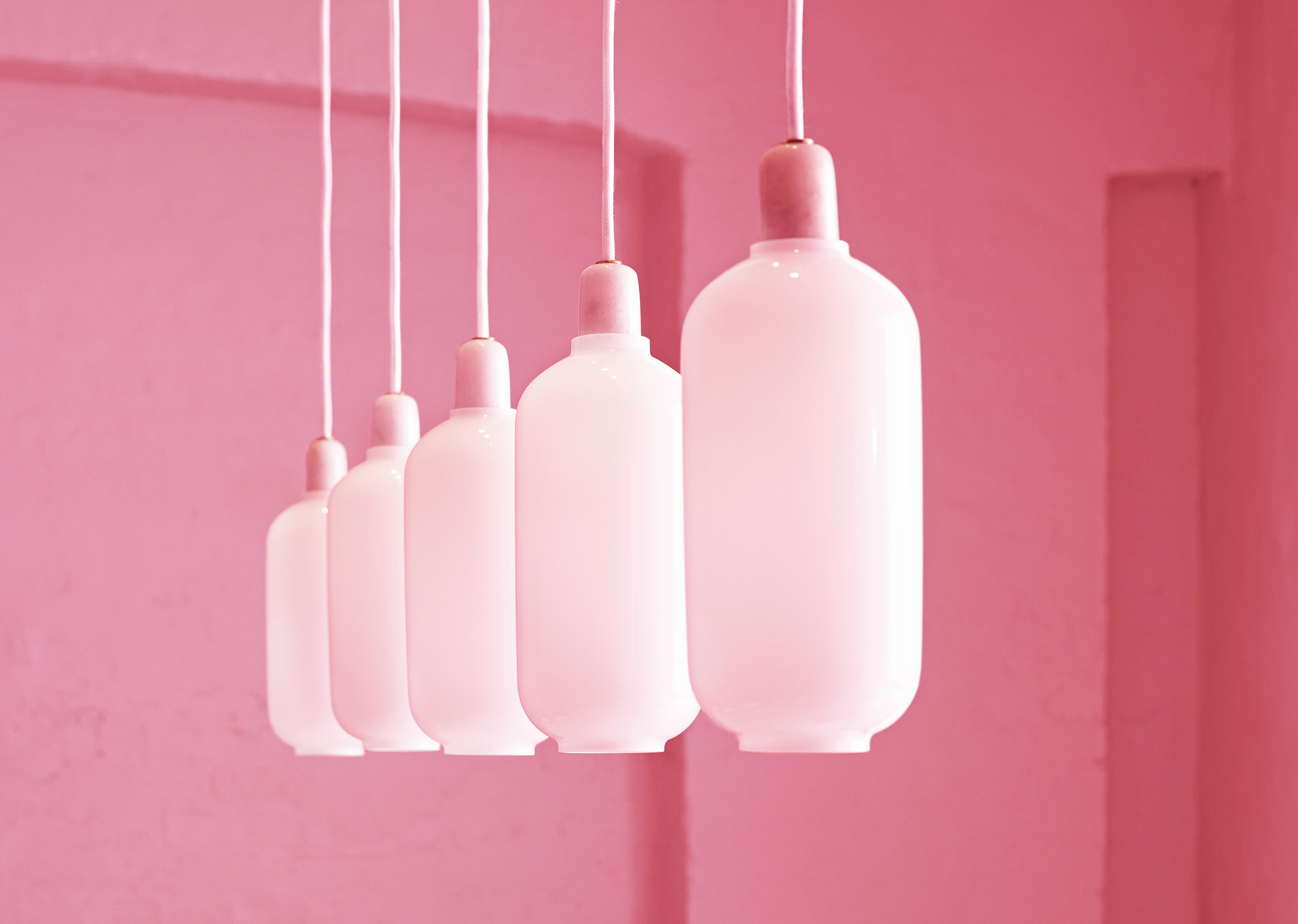 Reihe von weißen Amp Lamp Hängeleuchten von Normann Copenhagen vor rosa Hintergrund.