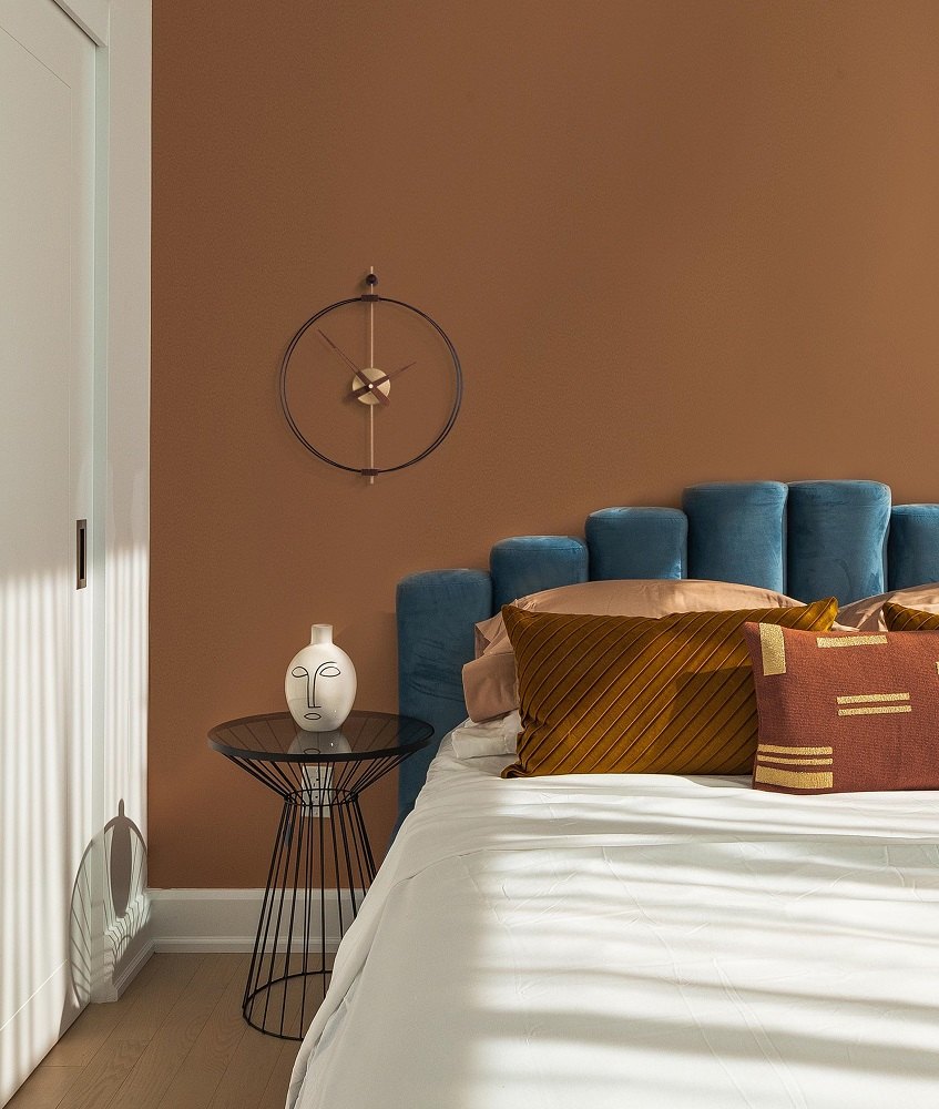 Schwarze Micro Barcelona Clock Wanduhr von nomon an brauner Wand über einem Bett im Schlafzimmer.