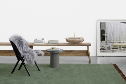 EC05 That Sessel e15 mit grauem Fell, Holztisch und grünem Teppich in minimalistischem Raum.