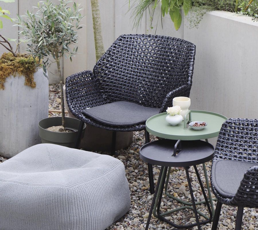 Cane-Line Vibe Highbacksessel aus Rattan mit grauem Sitzkissen und passendem Pouf im Garten.