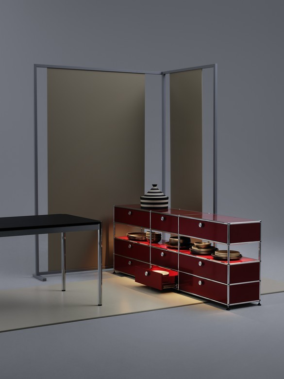 Rotes USM Haller Regal mit Glasböden und integrierter Beleuchtung, Schublade geöffnet, Geschirr sichtbar.