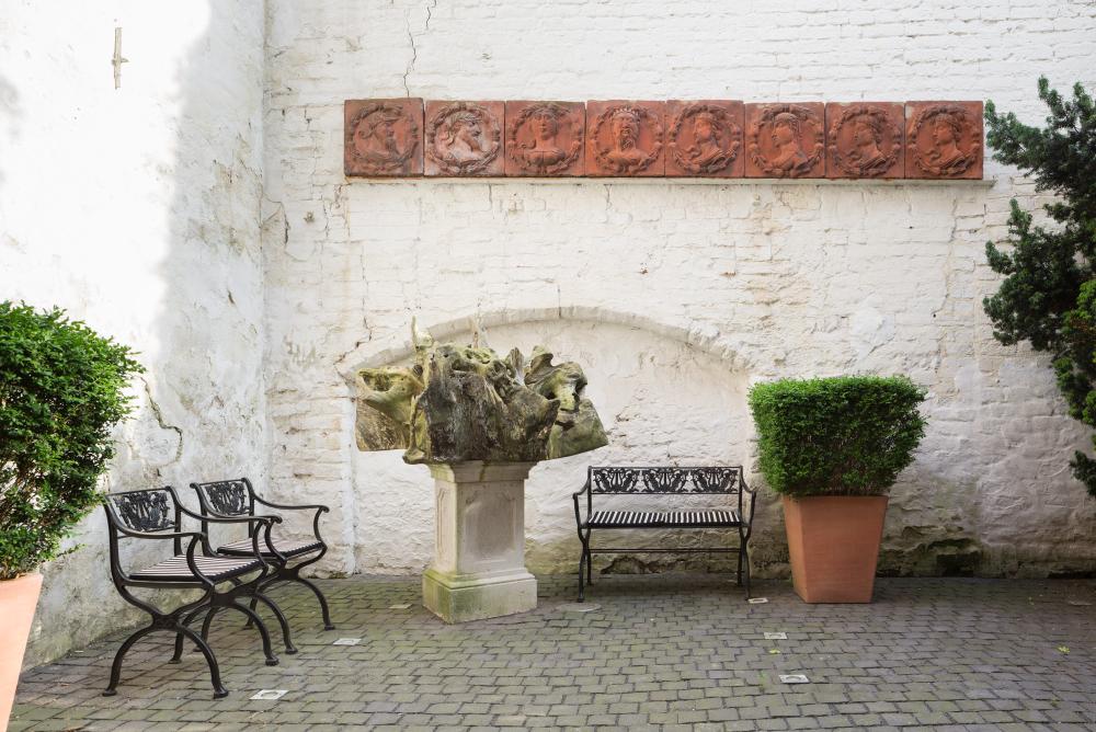Zwei schwarze D60 Gartensessel von Tecta im Außenbereich mit weißer Backsteinmauer und Skulptur.