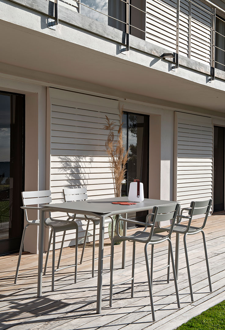 Graue Fermob Luxembourg Gartenmöbel: Tisch und Barhocker auf einer Holzterrasse im Außenbereich.