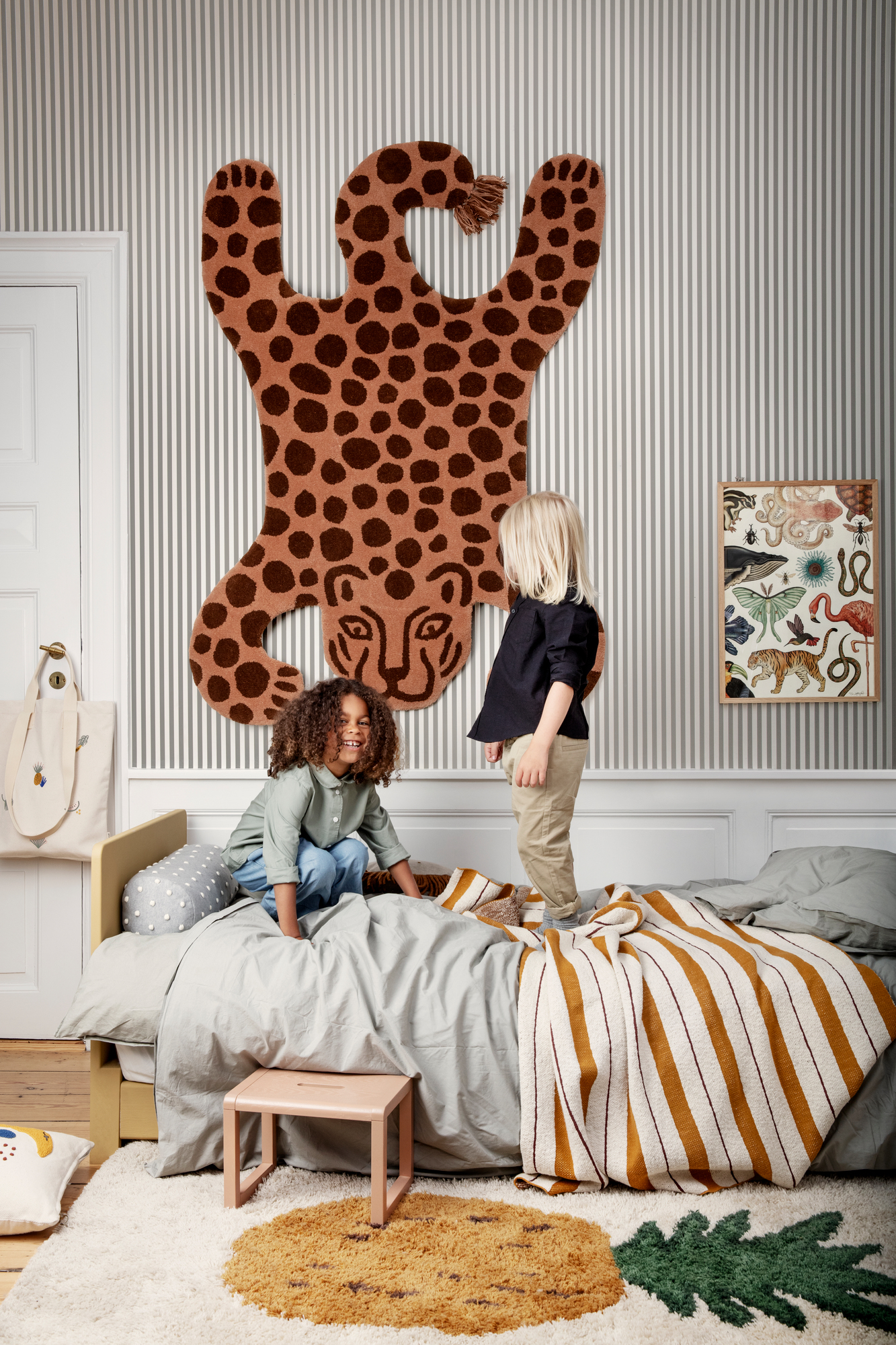 Kinderzimmer mit Ferm Living Safari Tufted Rug Leopard Teppich als Wanddeko, Kinder spielen auf Bett.