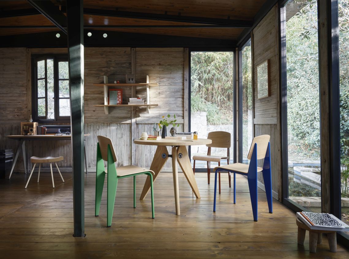 Innenaufnahme mit Vitra Wandregal aus Eiche und farbigen Stühlen. Modernes Design für Wohnzimmer und Büro.