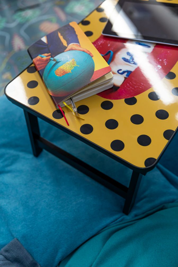 Toiletpaper Sofa Tray von Seletti, klappbarer Beistelltisch mit gelbem Punktmuster, Notizbuch und Tablet auf blauem Sofa.