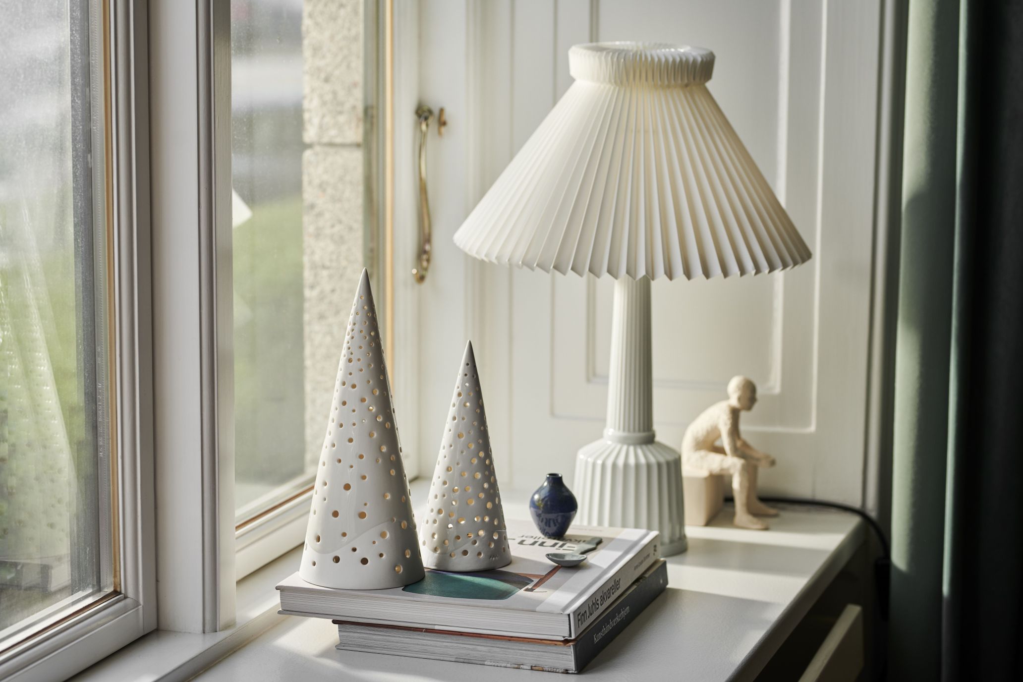 Zwei schneeweiße Nobili Teelichthalter von Kähler in Kegelform mit Lochmuster auf Büchern.