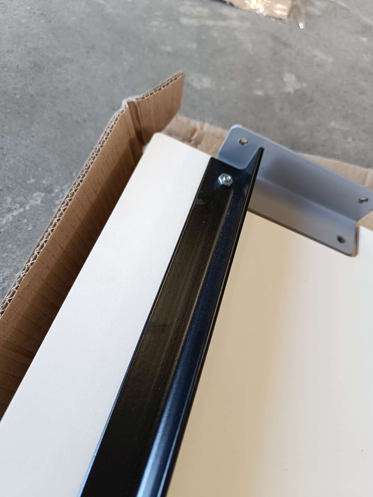 Detailaufnahme Stapelliege CPL Weiß (Mängelexemplar): Weiße Liegefläche mit schwarzem Rahmen und silberner Halterung im Karton.