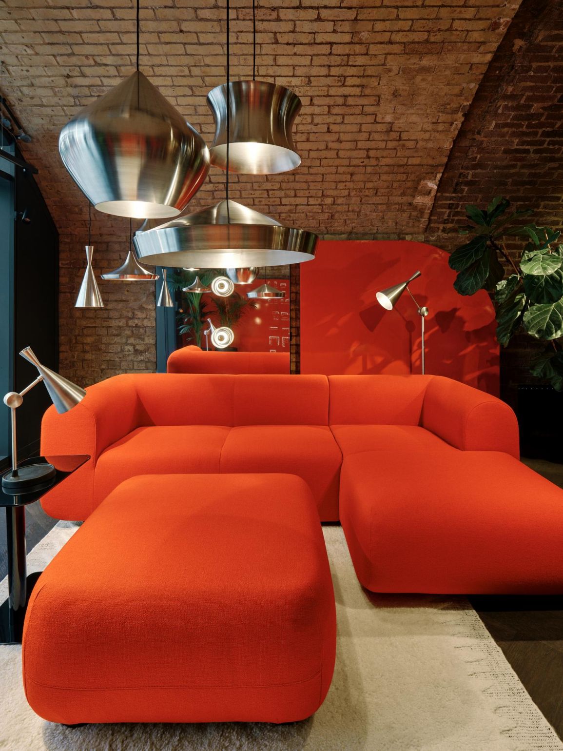 Mehrere Tom Dixon Unbeaten Pendelleuchten aus Metall hängen über einem orangefarbenen Sofa in einem Wohnzimmer.