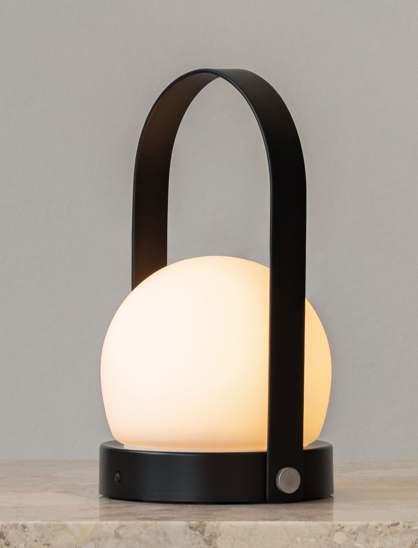 Carrie tragbare Tischleuchte: Akkuleuchte mit schwarzem Tragegriff und warmweißem Licht auf einem Tisch.