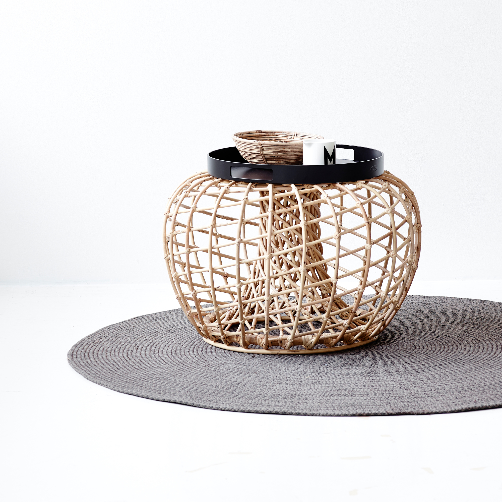 Nest Hocker von Cane-Line: Kleiner Beistelltisch aus Rattan mit schwarzer Glasplatte und Deko.