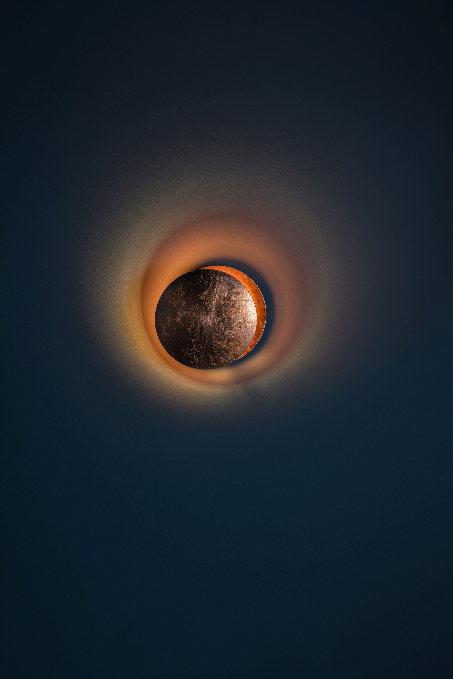 Lederam W Wandleuchte von Catellani & Smith in Gold und Kupfer an dunkler Wand.