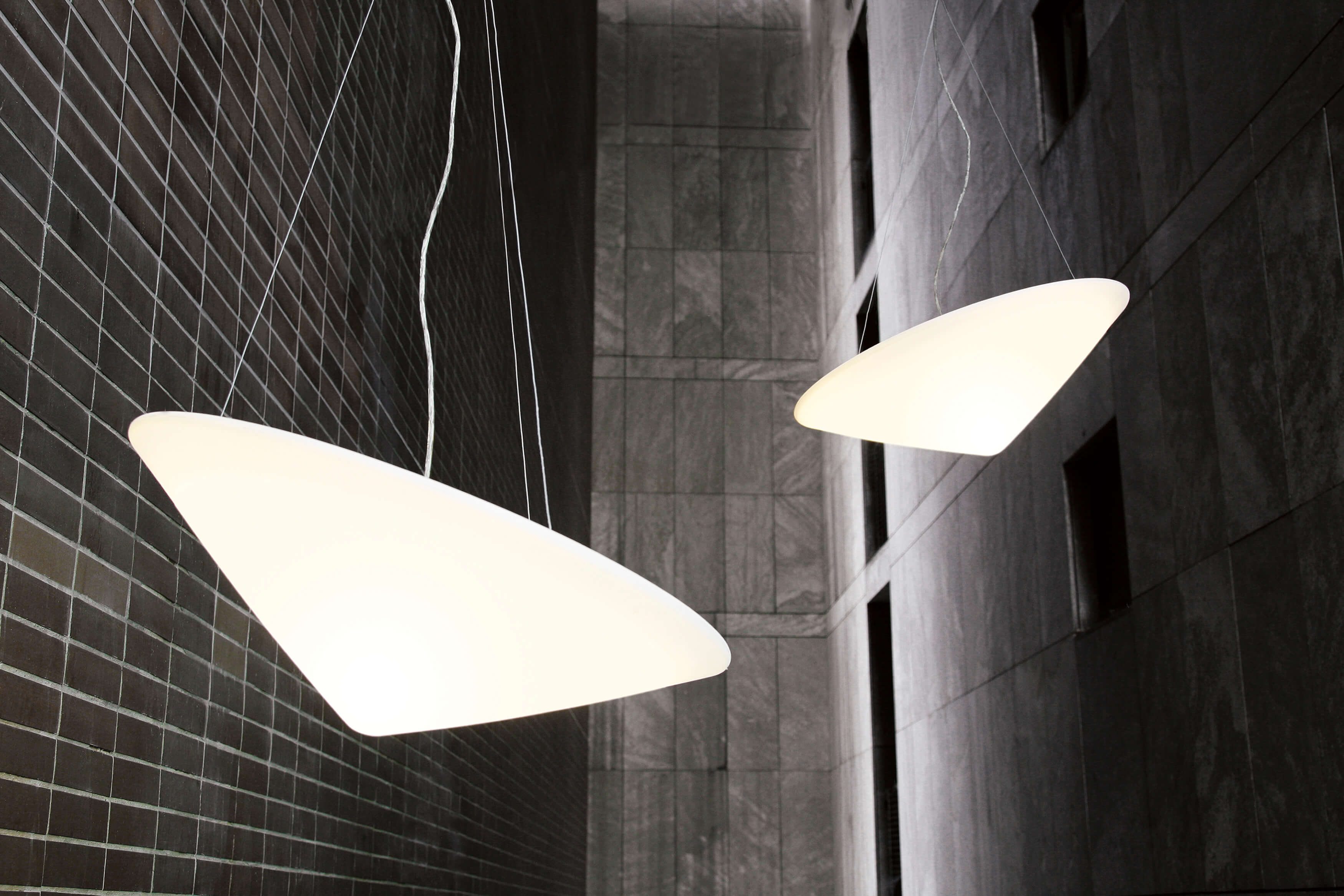 Zwei Cao Mao Pendelleuchten, modernes Design, weiße Leuchtenkörper, hängen vor einer dunklen Wand.