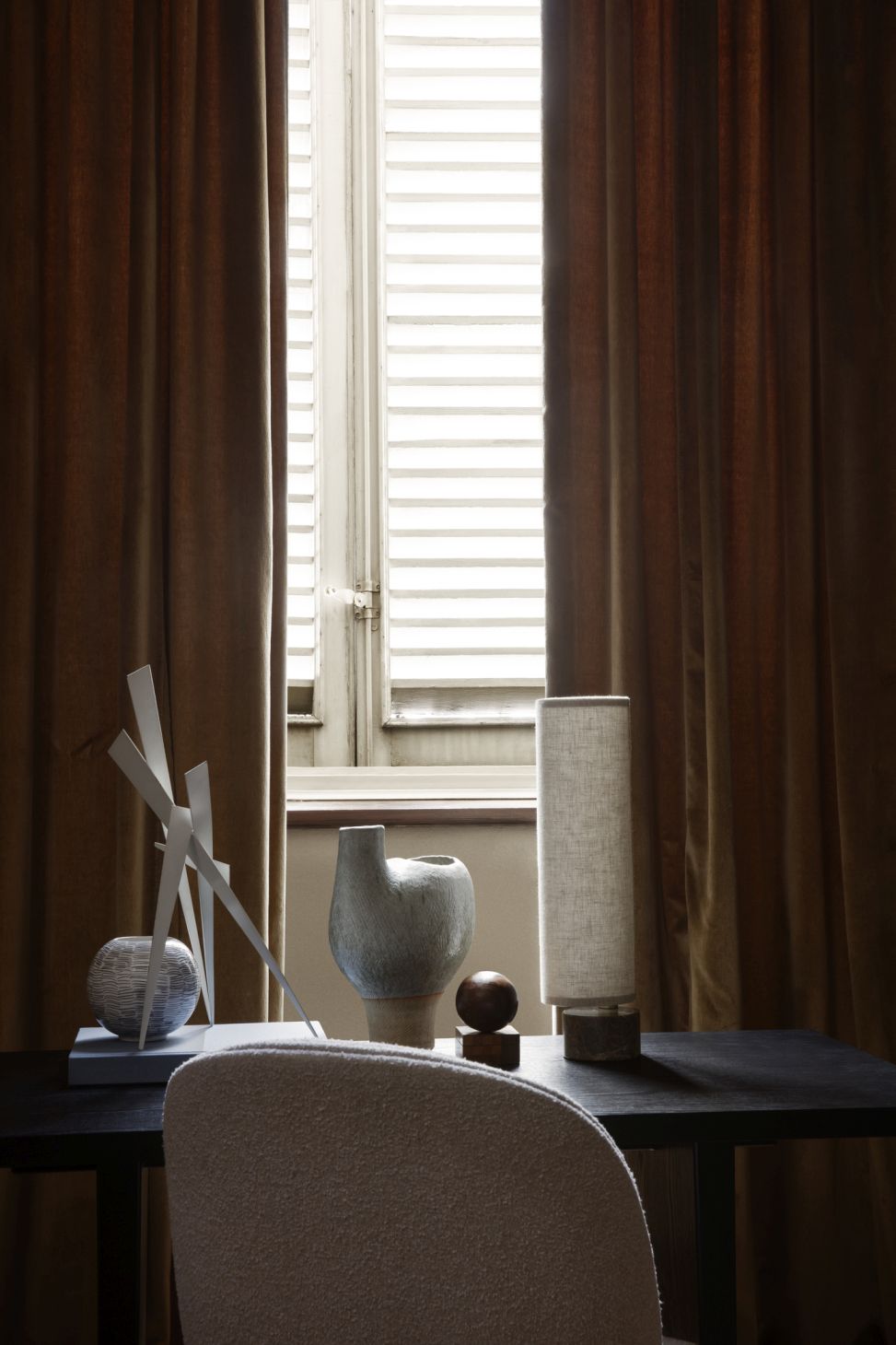 Detailaufnahme des Gubi Schreibtischs mit Dekoration vor einem Fenster mit braunen Vorhängen.