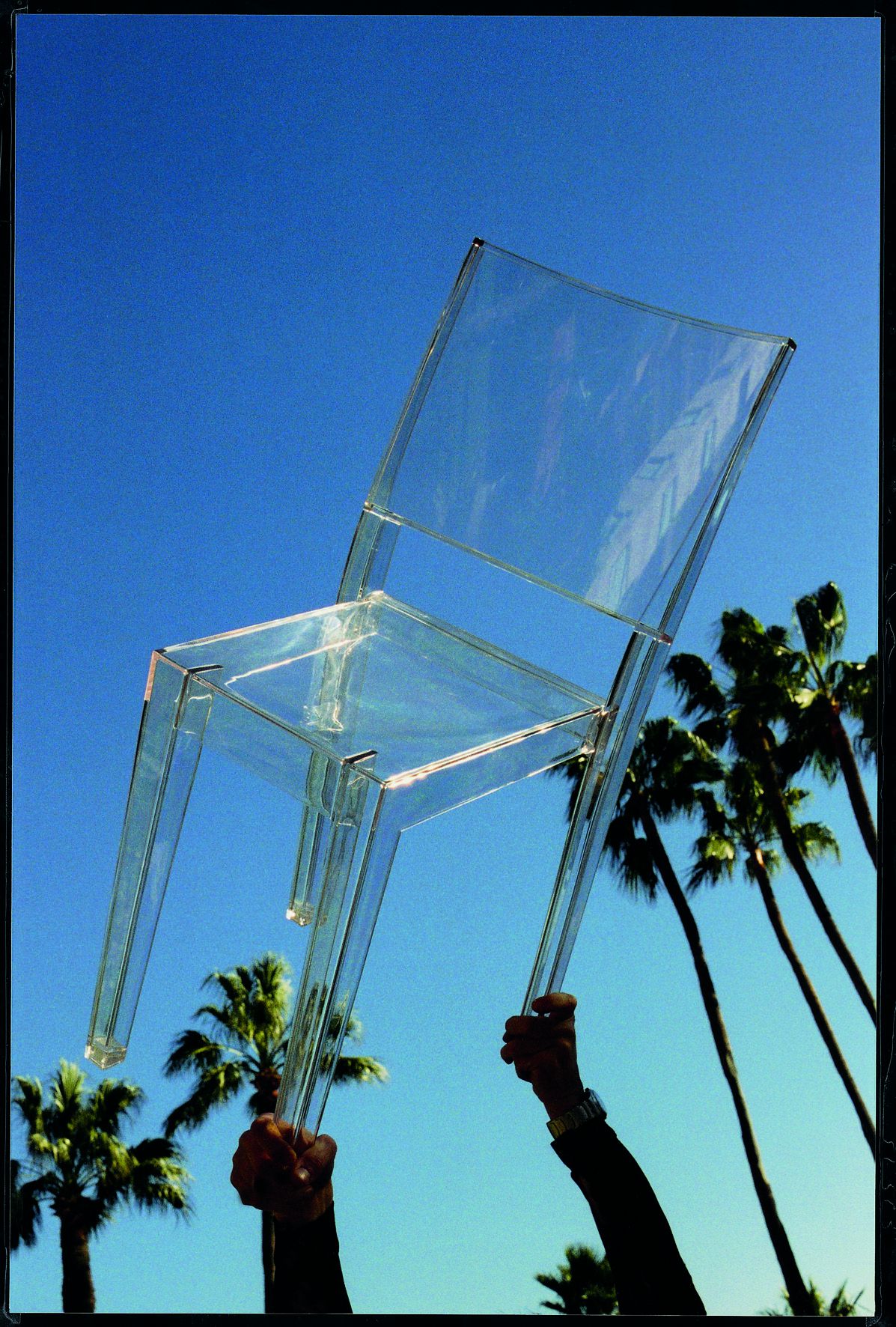 Transparenter La Marie Stuhl von Kartell, gehalten vor blauem Himmel und Palmen. Design Stuhl.