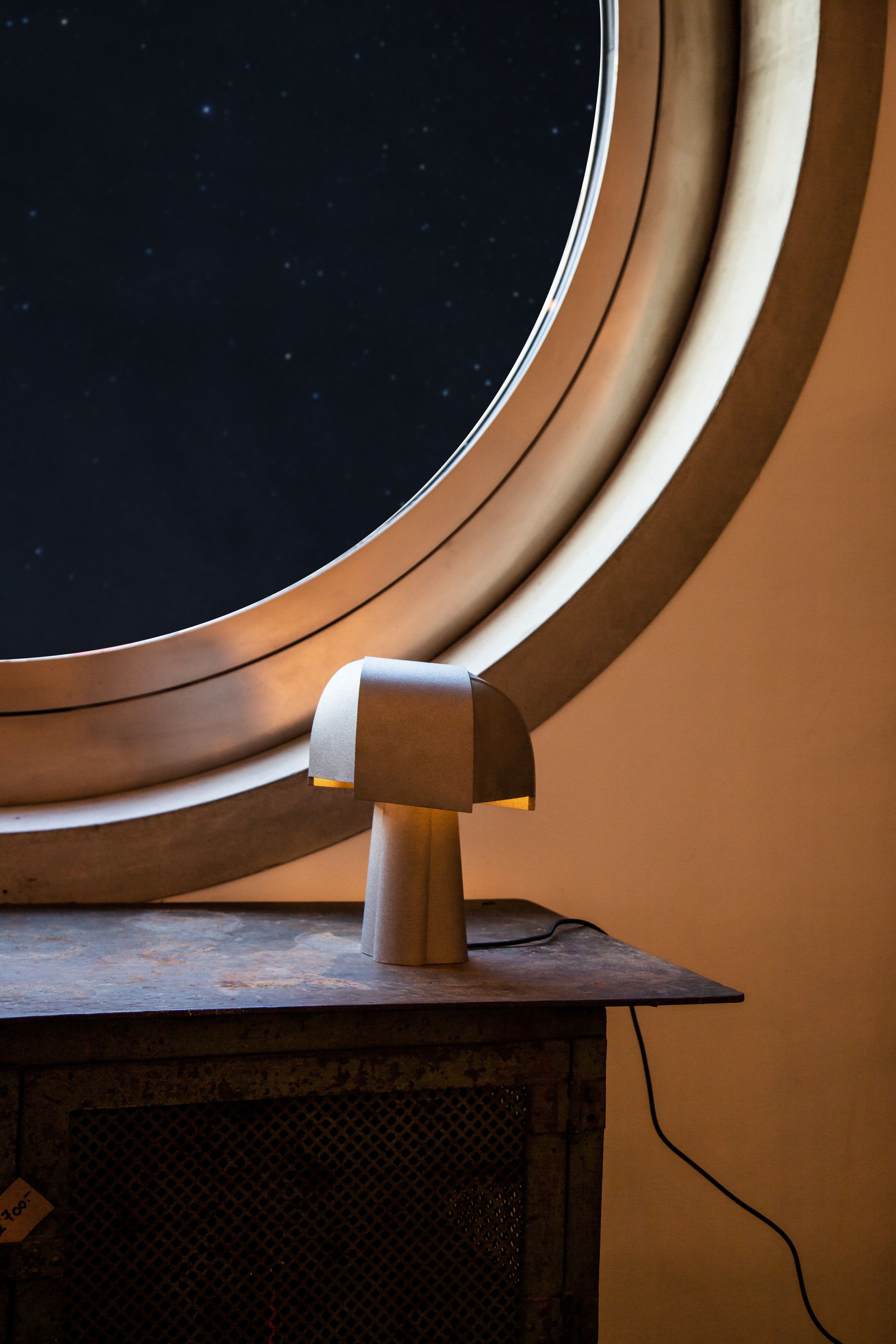 Samsa Tischleuchte von Pulpo, moderne Designleuchte aus Keramik, warmes Licht, vor rundem Fenster.