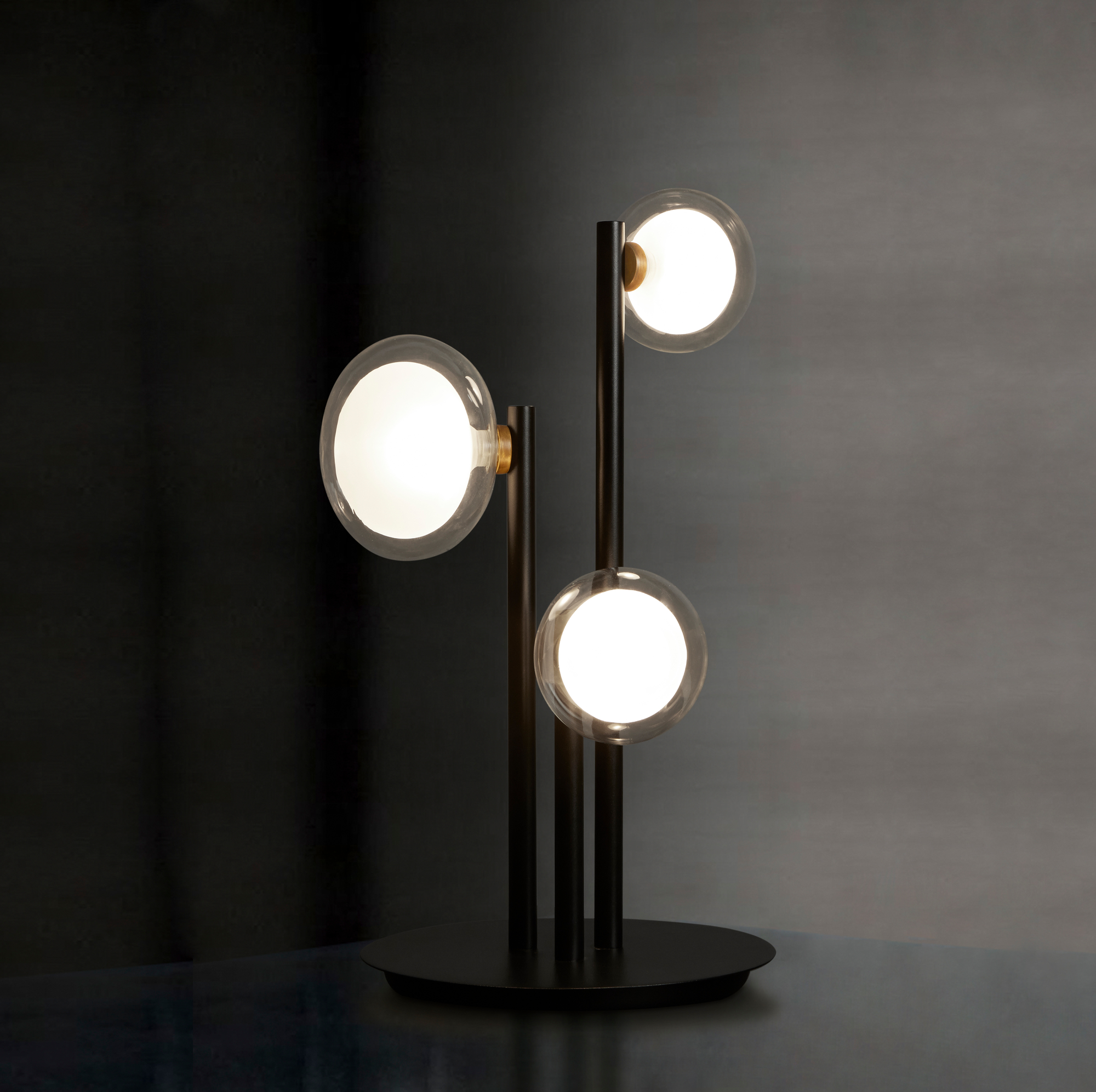 Nabila Tischleuchte von Tooy mit drei leuchtenden Glaskugeln und schwarzem Gestell.