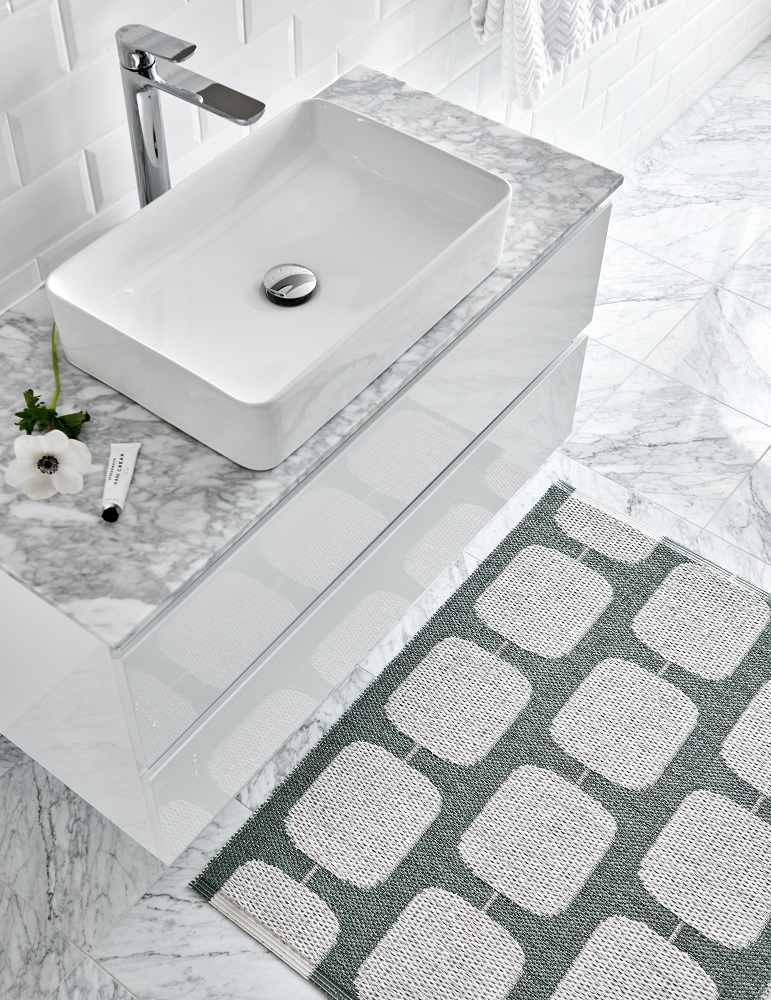 Sten Kunststoffteppich in Army/Fossil grau (Pappelina) neben einem Waschbecken im Badezimmer. Muster: Quadrate.