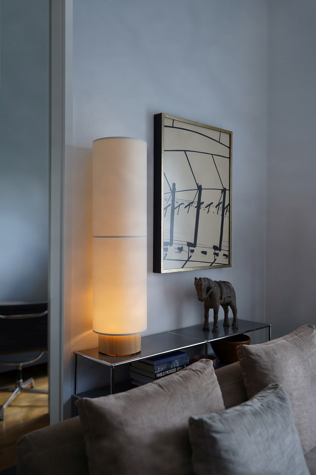 Hiro Stehleuchte von Maigrau, eine moderne Stofflampe auf einem Regal neben einem Sofa.