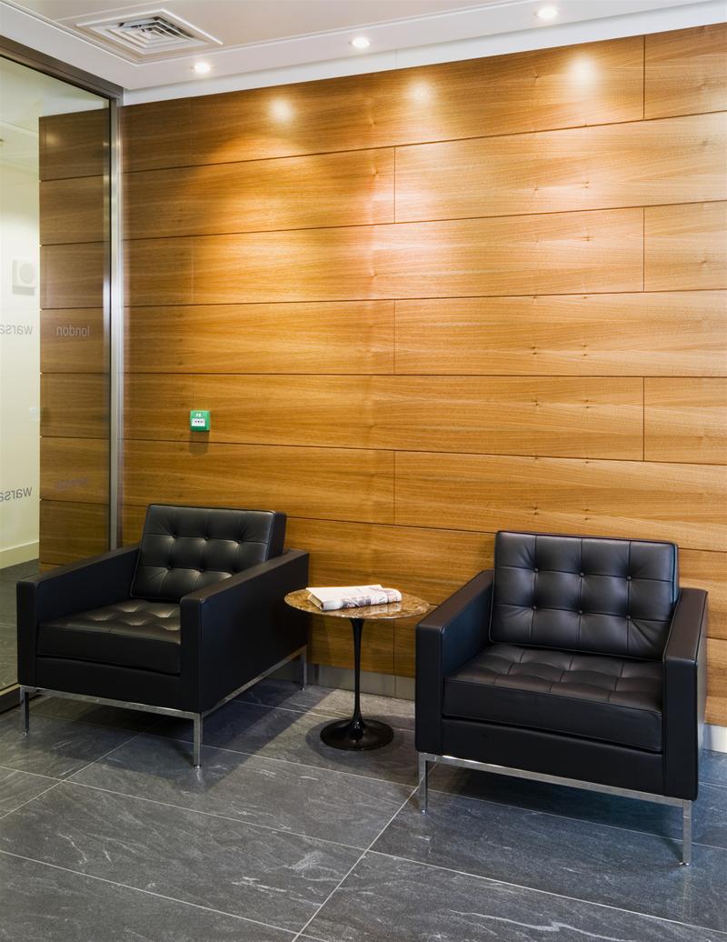 Zwei schwarze Florence RELAX Sessel von Knoll International mit Beistelltisch vor Holzwand.