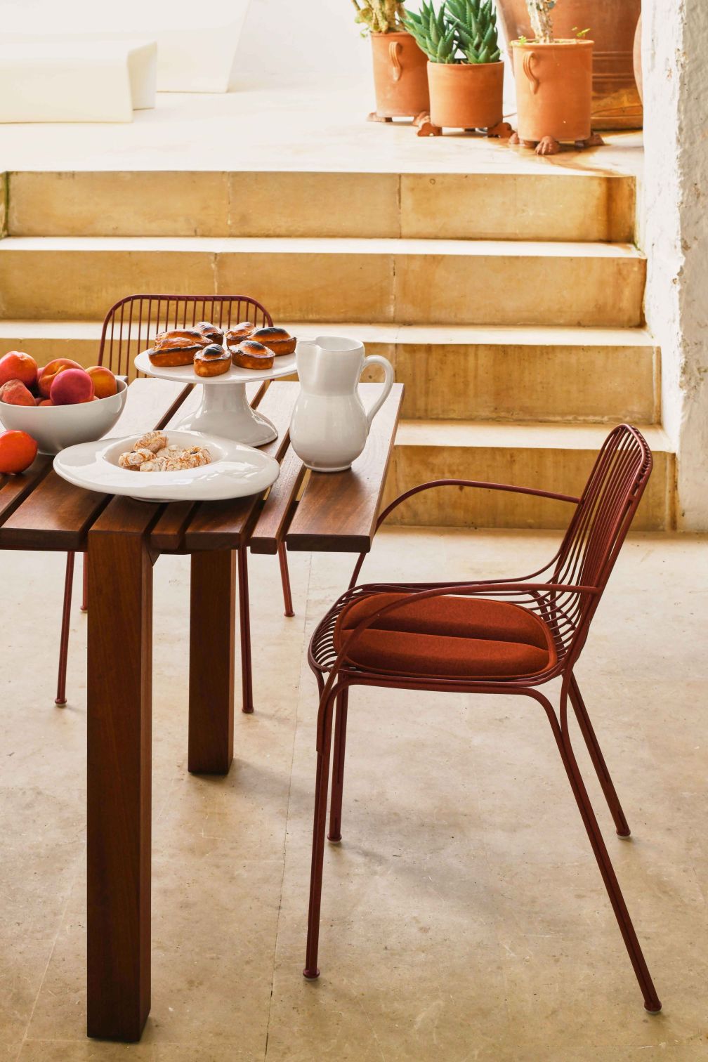 Roter Hiray Stuhl mit Armlehne von Kartell am Esstisch im Freien. Outdoor Möbel.