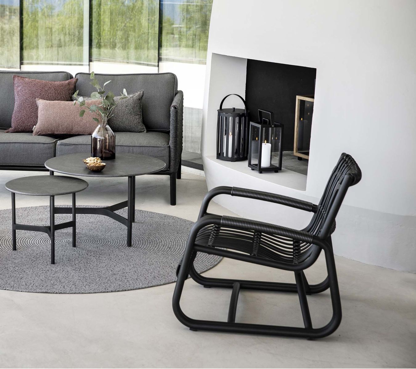 Lavagrauer Cane-Line Curve Loungesessel aus Rattan, Teil einer modernen Outdoor-Sitzgruppe mit Sofa und Tisch.