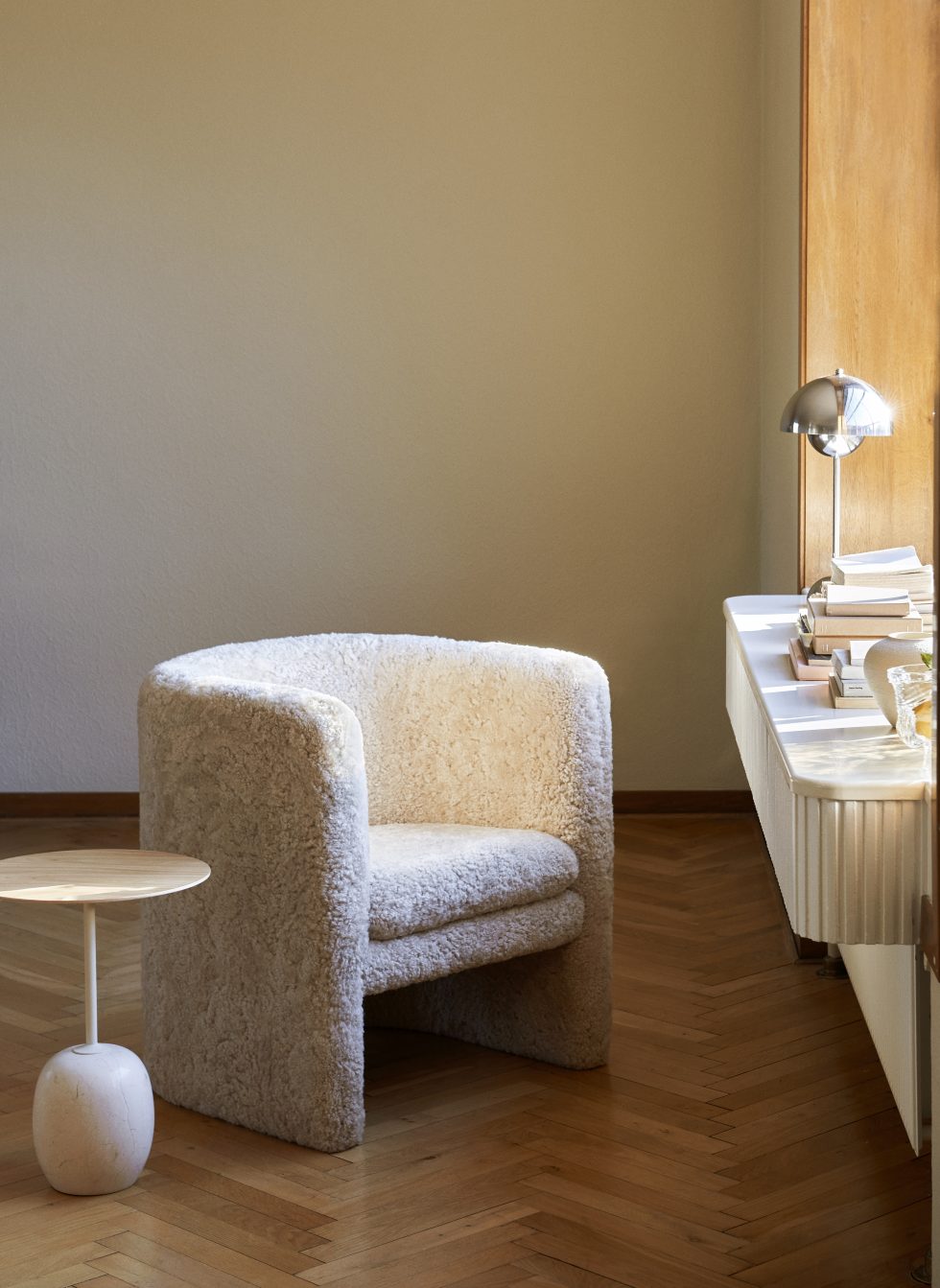 Lato Beistelltisch mit Holzplatte und Marmorfuß neben Sessel auf Parkettboden. AndTradition Design.