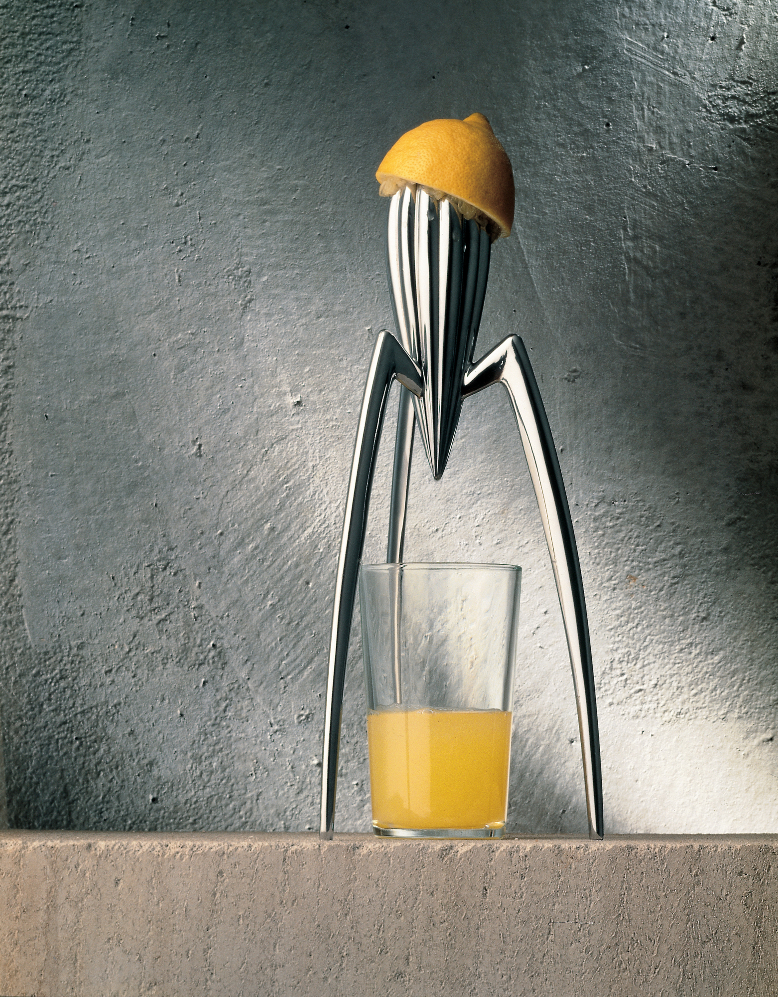 Alessi Juicy Salif Zitronenpresse aus Aluminium mit Zitrone und Glas Saft. Design-Zitruspresse.