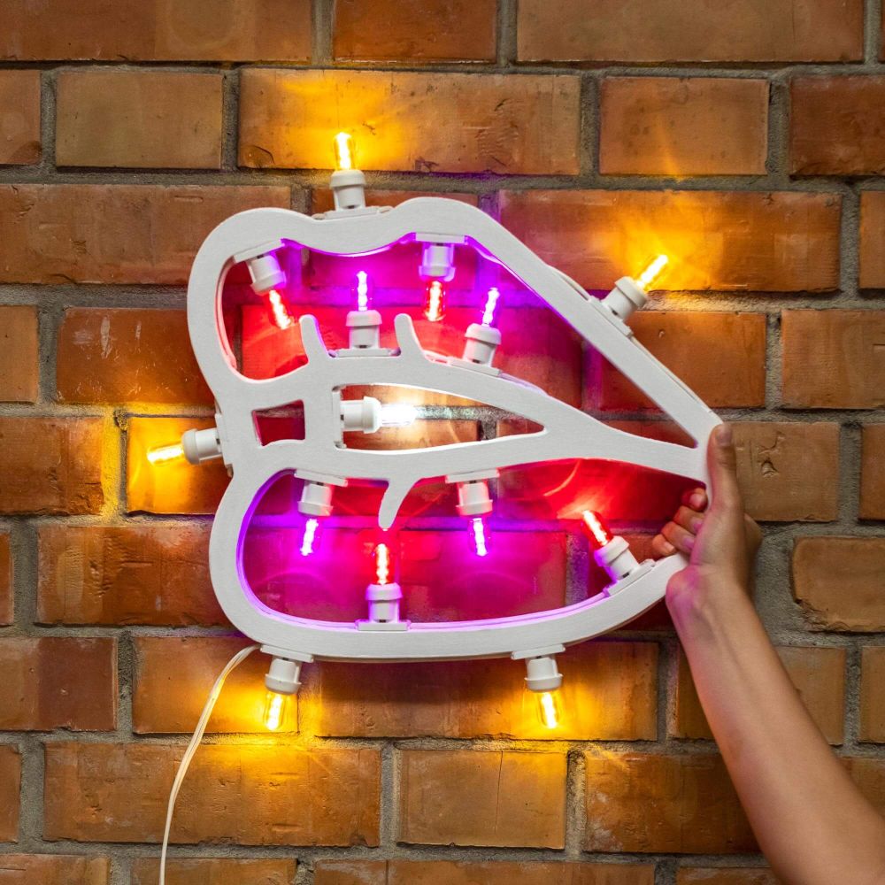 Weiße Lippen LED Leuchte von Seletti an einer Backsteinwand, mit gelben und pinken Lichtern.