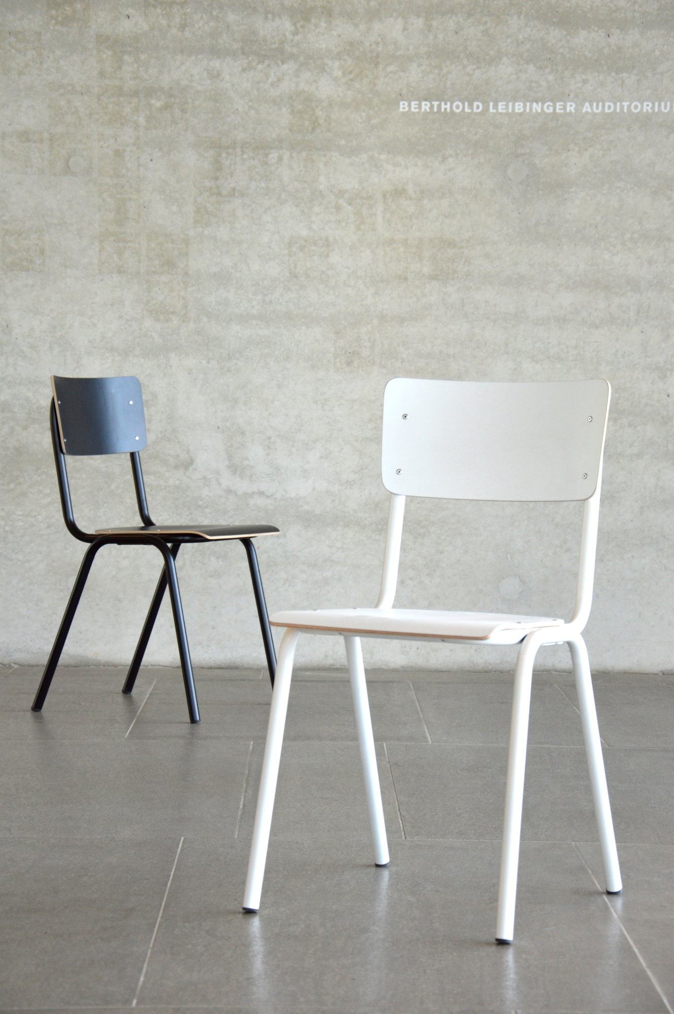 Zwei Jan Kurtz Zero Stühle, einer schwarz und einer weiß, vor einer Betonwand.