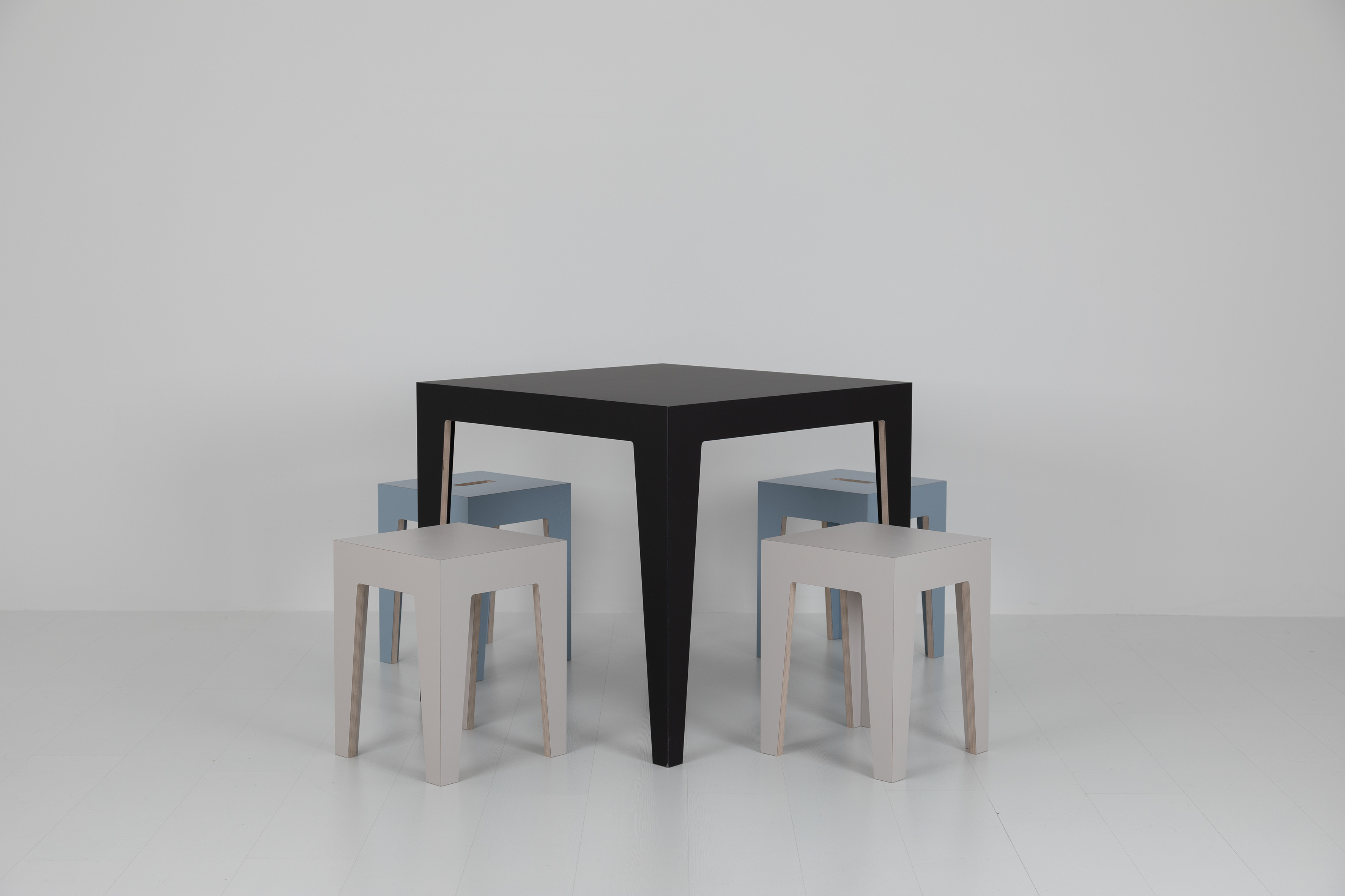 Schwarzer MARTA Holztisch mit vier Hockern in Grau und Blau vor weißem Hintergrund.