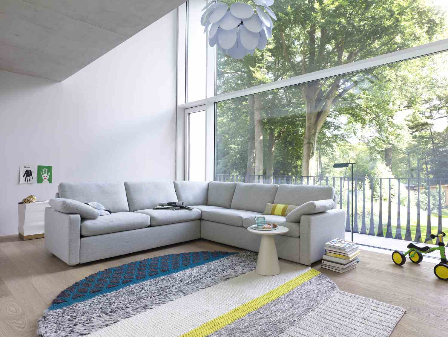 Helles Wohnzimmer mit grauem Conseta Sofa, Ecksofa, Teppich und großer Fensterfront. Modernes Wohnen.