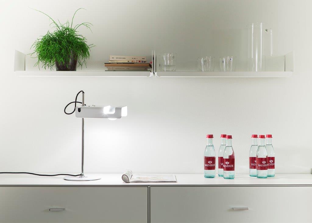 Weiße Spider Tischleuchte von Oluce auf einem weißen Tisch mit Wasserflaschen und Dekoration.