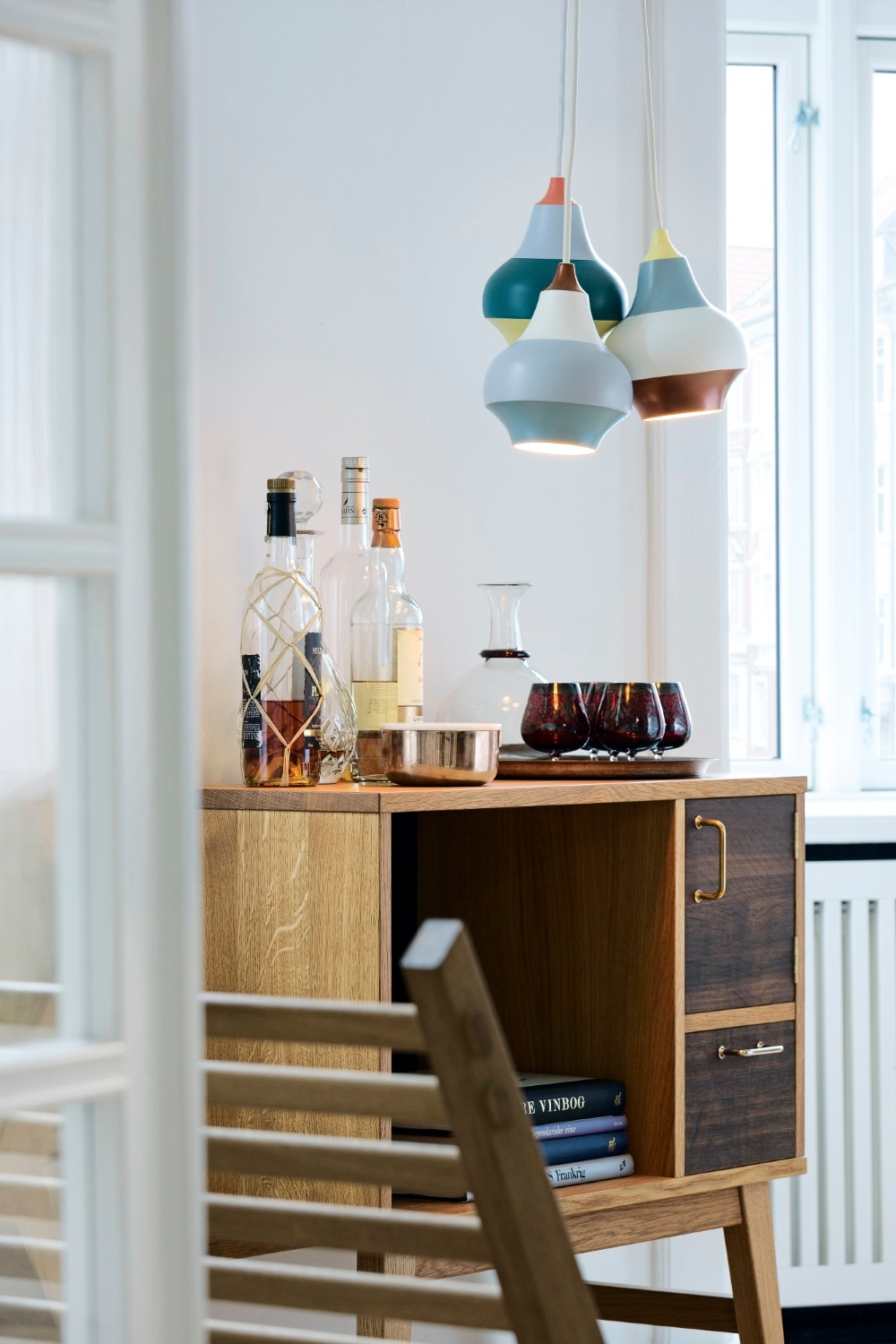 Drei farbenfrohe Louis Poulsen Cirque Pendelleuchten über einem Sideboard mit Flaschen und Gläsern.