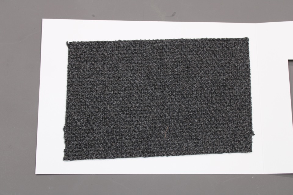 Stoffmusterkarte Gruppe 82 Cor: Nahaufnahme eines grauen, texturierten Möbelstoff-Musters auf weißem Karton.