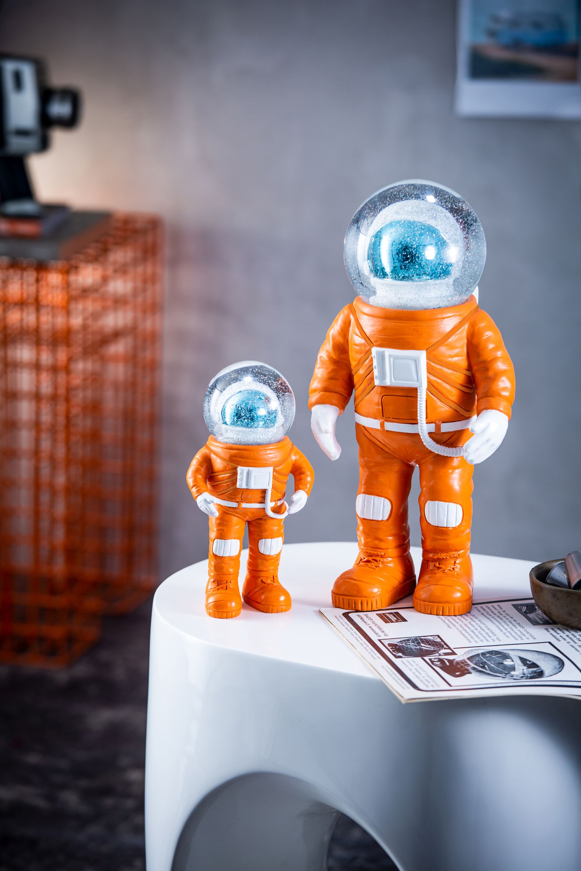 Zwei orangefarbene Marstronaut Glitzerkugeln von Summerglobes, Einzelstücke, auf einem weißen Tisch. Dekorative Schneekugel mit Astronauten.
