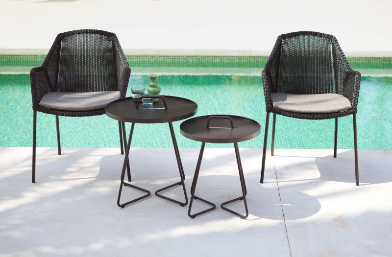 Cane-Line Breeze Outdoor Stuhl mit Kissen und Beistelltischen am Pool.