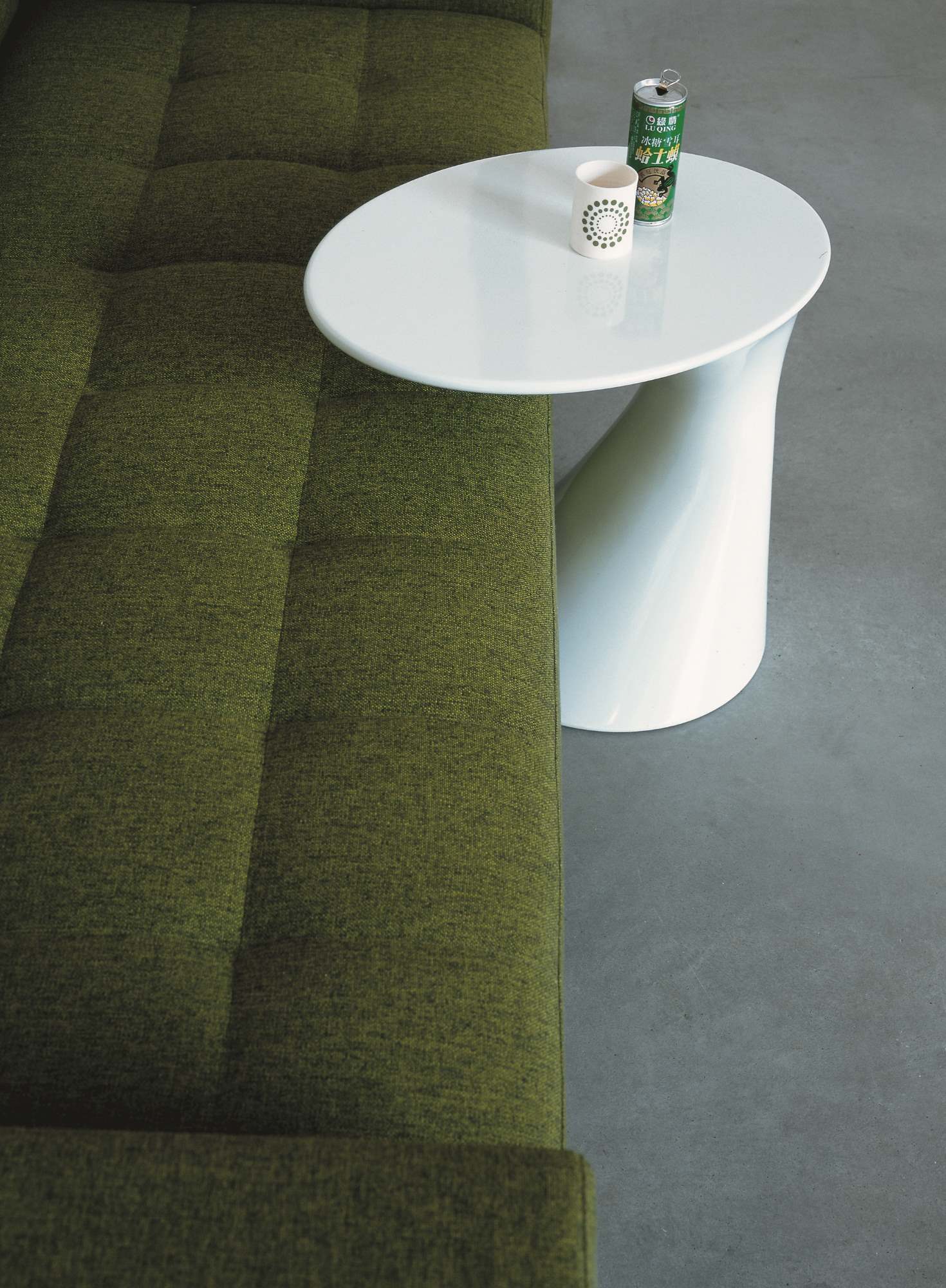 Detailaufnahme des Zanotta Tod Couchtischs mit Getränken auf einer weißen, runden Tischplatte neben einem grünen Sofa.