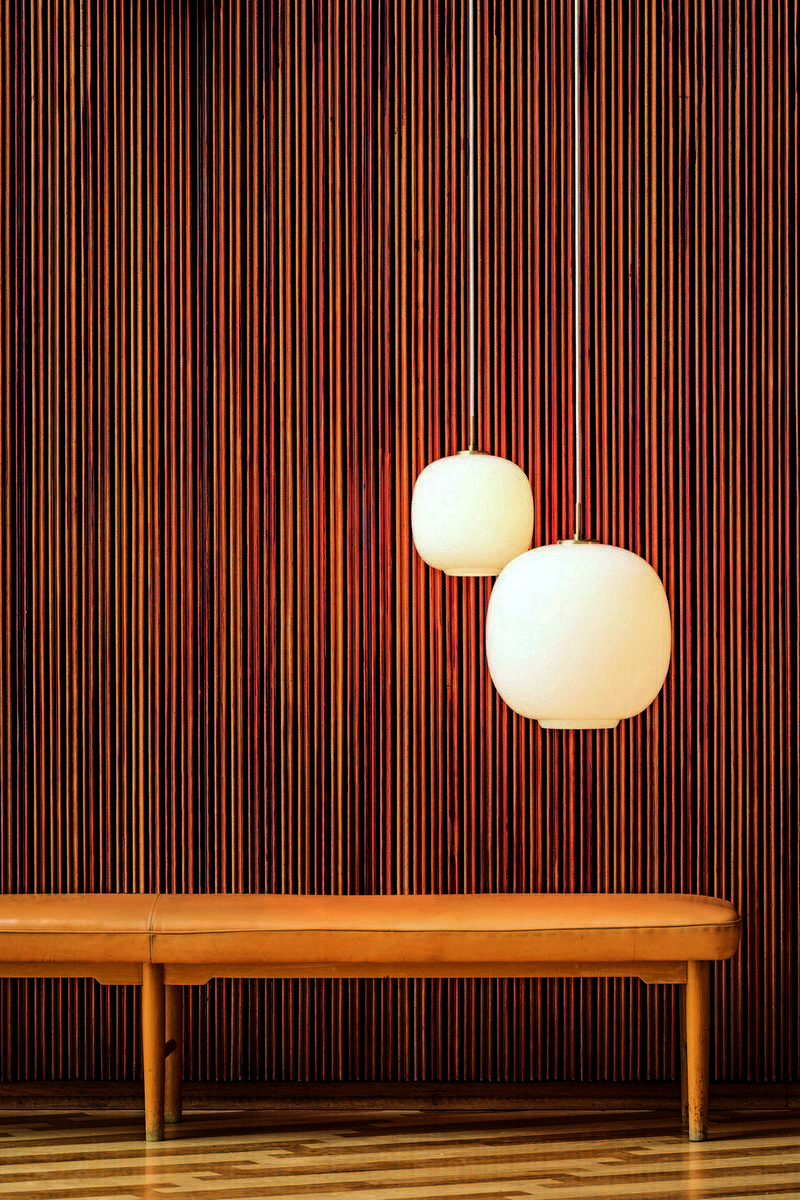 Zwei VL45 Radiohus Pendelleuchten von Louis Poulsen, weiße Glaslampen hängen vor einer Holzvertäfelung und einer Bank.