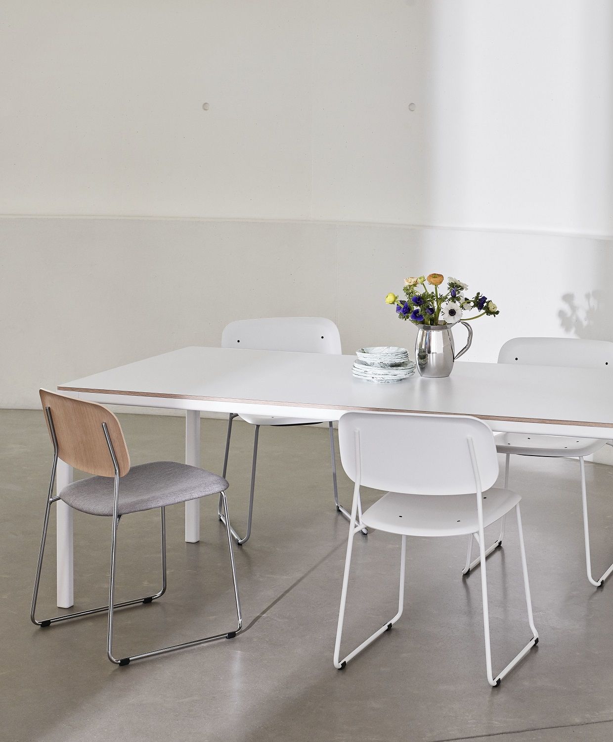 Esstisch mit vier Hay Soft Edge Stühlen, davon einer mit grauem Sitzpolster und Holzlehne.