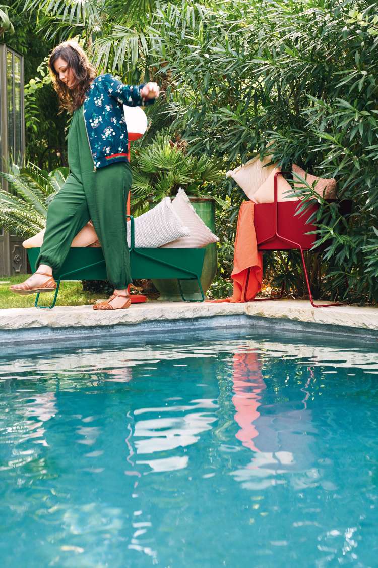 Fermob Basket Blumenkasten lang in Grün und Rot neben Pool mit Kissen und Textilien.