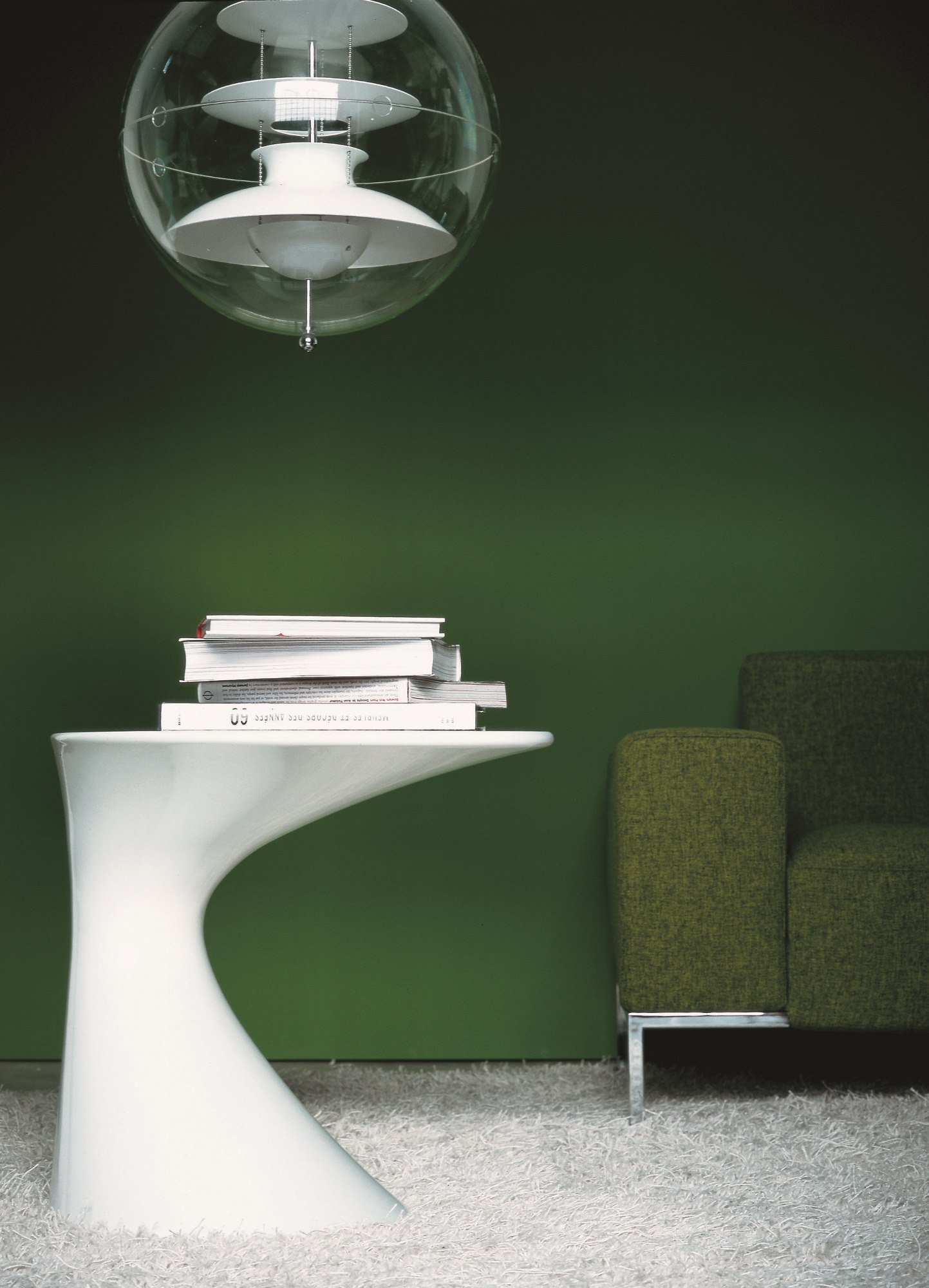 Weißer Zanotta Tod Couchtisch mit Büchern, Stehlampe und grünem Sofa auf einem weißen Teppich.